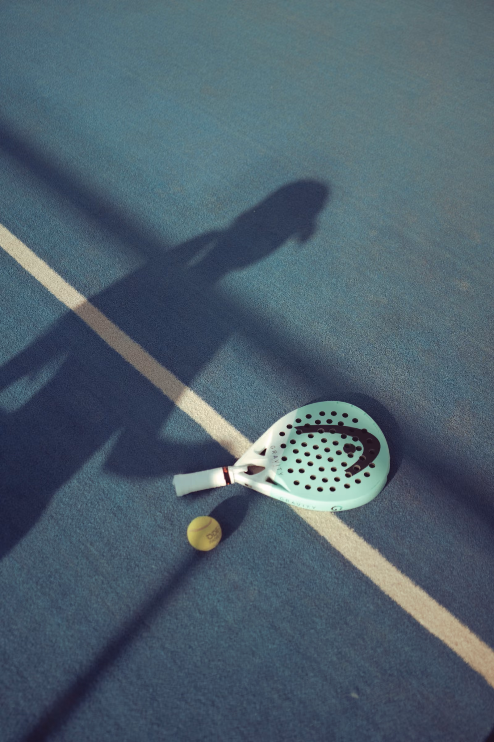 Raquette et balle de padel posées sur la piste